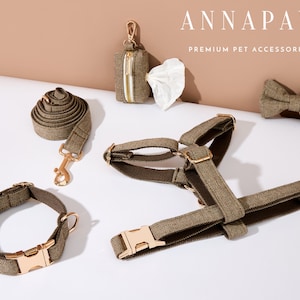 Può includere: Un set di accessori per cani di colore marrone e oro, tra cui un guinzaglio, un collare, un imbracatura, un porta sacchetti per la cacca e un papillon. Gli accessori sono realizzati in tessuto a spina di pesce e hanno accessori dorati. Il testo "ANNAPAW PREMIUM PET ACCESSORIES" è visibile nell'immagine.