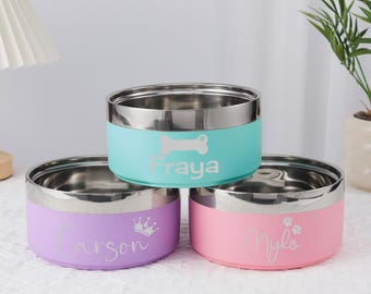 May include: Three stainless steel pet bowls in pastel colors: light blue, lavender, and pink. Each bowl has a silver rim and a personalized name with a graphic. The light blue bowl has a bone graphic, the lavender bowl has a crown, and the pink bowl has paw prints.