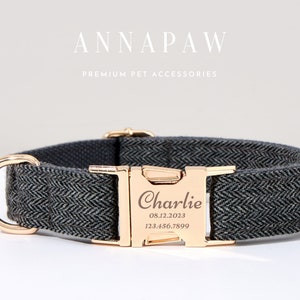 May include: A grey herringbone dog collar with gold-coloured metalwork. The collar has a gold buckle engraved with the name "Charlie", a date, and a phone number. The brand name "ANNAPAW" is displayed above the collar.