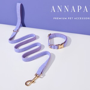 May include: A lavender pet leash and collar set with gold hardware. The leash is coiled and the collar is laying flat. The text "ANNAPAW PREMIUM PET ACCESSORIES" is visible in the background.