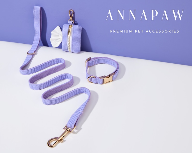 May include: A lavender pet leash, collar, and poop bag holder with gold hardware. The leash and collar are made of a soft, textured fabric. The poop bag holder has a zipper closure. The text "ANNAPAW PREMIUM PET ACCESSORIES" is displayed above the products.