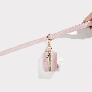 Puede incluir: Un porta bolsas para excrementos de perro de terciopelo rosa con una cremallera dorada y un clip dorado unido a una correa de terciopelo rosa.