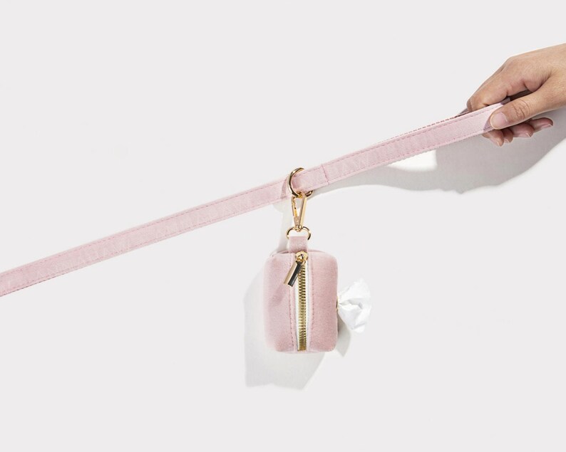 Puede incluir: Un porta bolsas para excrementos de perro de terciopelo rosa con una cremallera dorada y un clip dorado unido a una correa de terciopelo rosa.