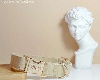 May include: A beige dog collar with a gold buckle that says "MILO" on it. The collar is on a wooden surface.