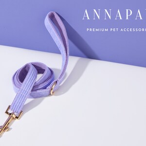 May include: A lavender corduroy dog leash with a gold metal clasp.  ANNAPAW PREMIUM PET ACCESSORIES is printed in white text on a purple background.