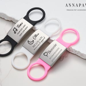 Pode incluir: Três etiquetas de identificação para animais de estimação personalizadas com anéis de silicone preto, branco e rosa. As etiquetas são gravadas com os nomes Gus, Ollie e Bonnie, juntamente com números de telefone e informações sobre o microchip.