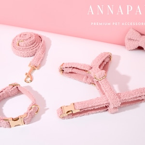 K&ouml;nnte beinhalten: Ein rosa flauschiges Hundegeschirr, Halsband und Fliege. Das Set besteht aus weichem, pl&uuml;schem Material und verf&uuml;gt &uuml;ber goldene Beschl&auml;ge. Der Text "ANNAPAW PREMIUM PET ACCESSORIES" ist in der oberen rechten Ecke des Bildes sichtbar.