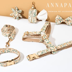 May include: A collection of pet accessories with a floral pattern, including a collar, leash, harness, bow tie, flower, and waste bag dispenser. The accessories have gold-colored hardware and are arranged on a white surface.