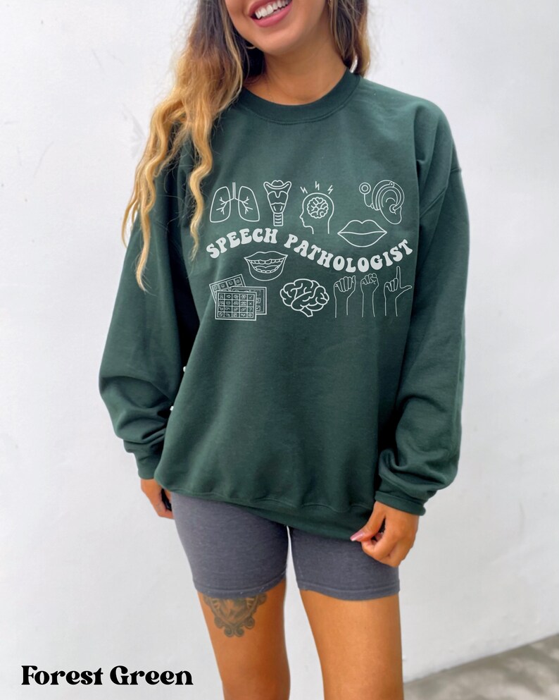 Puede incluir: Sudadera verde bosque con ilustraciones blancas de contorno de s&iacute;mbolos de pat&oacute;logo del habla y el texto "SPEECH PATHOLOGIST".
