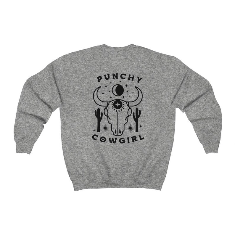 May include: Gray sweatshirt with a black graphic of a cow skull with a third eye, surrounded by stars and cacti. The text "Punchy Cowgirl" is below the skull.