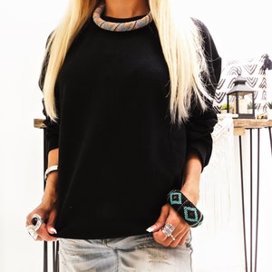 May include: A black long-sleeved sweatshirt with a colorful beaded necklace and a black and turquoise beaded bracelet.