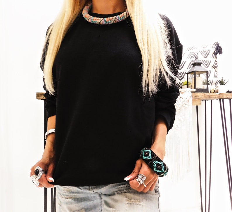 May include: A black long-sleeved sweatshirt with a colorful beaded necklace and a black and turquoise beaded bracelet.