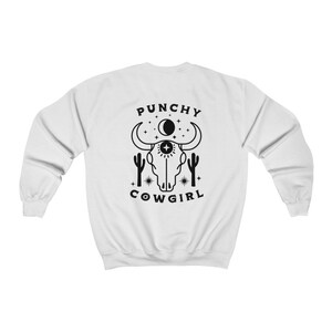 May include: White sweatshirt with a black graphic of a skull with horns, a crescent moon, stars, and cacti. The text "PUNCHY COWGIRL" is below the graphic.