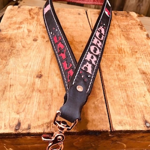 May include: A black leather strap with a pink and red "LYLA" and "AURORA" inscription. The strap has a copper-colored metal clip.