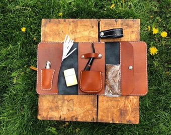 Puede incluir: Una bolsa de tabaco de cuero marrón con múltiples compartimentos. La bolsa tiene un bolsillo con cremallera, un bolsillo para un encendedor, un bolsillo para una pipa y un bolsillo para tabaco. La bolsa está sobre una superficie de madera.