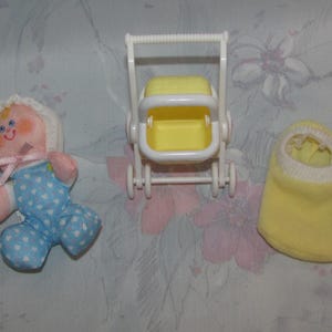 May include: A vintage toy set featuring a doll, a stroller, and a shoe. The doll has a pink face, a white bonnet, and a blue and white patterned outfit. The stroller is white with a yellow seat. The shoe is yellow.