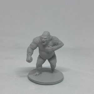 Könnte beinhalten: Graue Miniatur-Gorilla-Figur mit detaillierter Fellstruktur. Der Gorilla steht aufrecht, der Mund ist geöffnet und eine Hand liegt auf der Brust. Die Figur steht auf einem kleinen, runden Sockel.