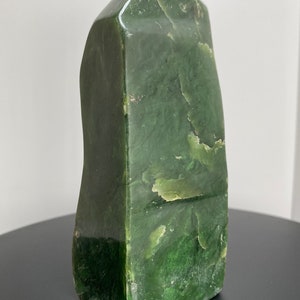 May include: A green nephrite jade stone carved into a tall, pointed shape. The stone has a smooth, polished surface and a natural, organic texture.