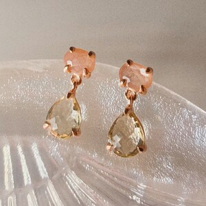 May include: A pair of gold earrings with a teardrop-shaped light green gemstone and a smaller pink gemstone above it.