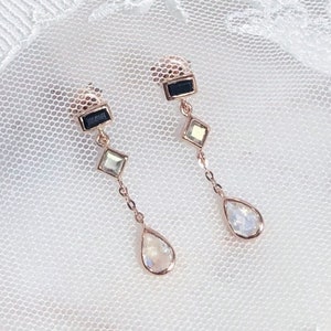 May include: A pair of gold dangle earrings with a black square, a clear square, and a teardrop-shaped crystal.