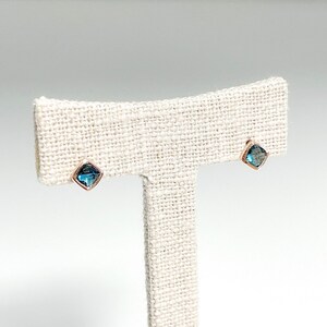 May include: A pair of small, square-shaped earrings with blue gemstones set in gold.