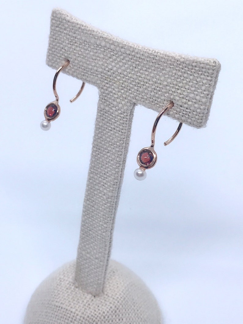May include: A pair of gold hoop earrings with a small red gemstone and a pearl dangling from each hoop.