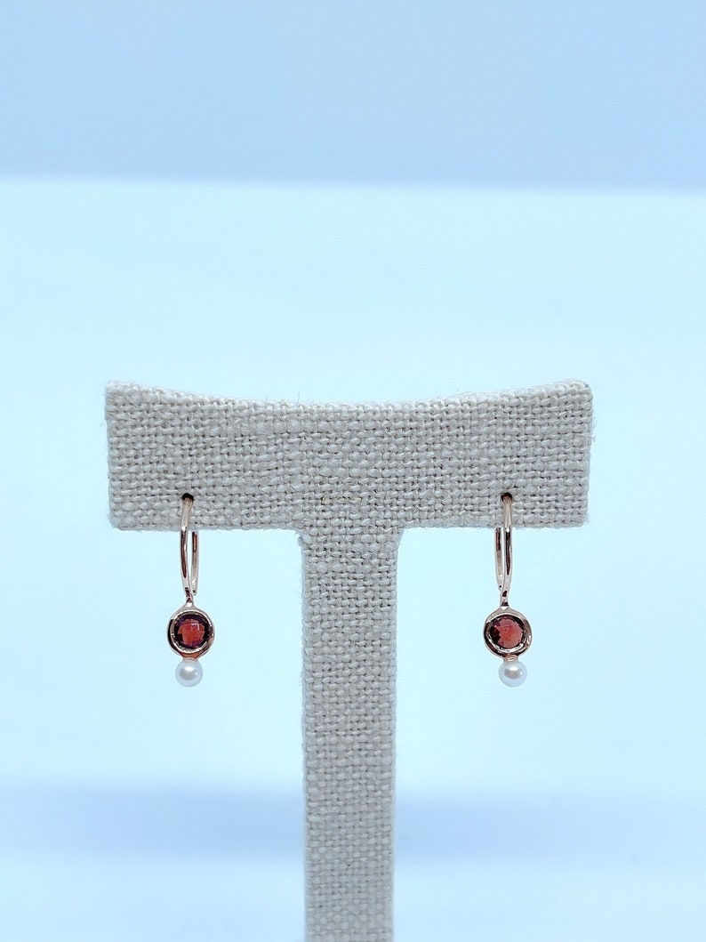 May include: A pair of gold hoop earrings with a small red gemstone and a pearl dangling from each hoop.