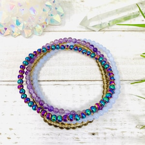 Anti Anxiety Crystal Bracelets 4mm round beads of Amethyst, Blue Lace Agate, Smoky Quartz, Rainbow Hematite on white wooden plank. Dainty stackable crystal bracelet design with intention of relieving stress and worry.