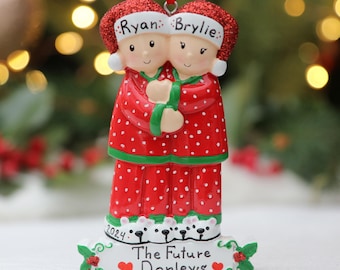 May include: A personalised Christmas bauble featuring a couple in red and white pyjamas with the names "Ryan" and "Brylie" on their hats. The bauble also includes the text "The Future Donleys" and the year "2024".