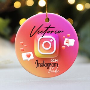 May include: A pink and orange Christmas ornament with the text "Victoria 2024 Instagram Babe" and a stylized Instagram icon.