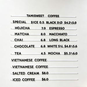 Puede incluir: Un menú blanco montado en la pared con texto negro que enumera las opciones de café y té. Los elementos del menú incluyen espresso, matcha, chai, moca y café vietnamita. Los precios se enumeran junto a cada artículo.