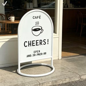 Puede incluir: Un letrero de café blanco arqueado con texto negro y un gráfico de taza de café. El letrero dice "CAFÉ", un icono de taza de café y "CHEERS!". Debajo, indica "OPEN AM8:30-PM20:00". El letrero está sobre un marco de metal blanco.