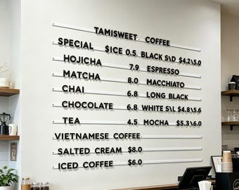 Puede incluir: Un menú de cafetería con el texto "TAMISWEET. COFFEE". El menú enumera varias opciones de café y té, con precios. El tablero está montado en una pared blanca.