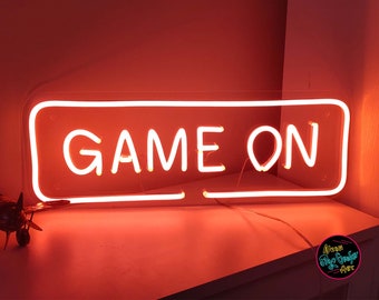 Puede incluir: Un letrero de neón con un contorno blanco y un fondo rojo. El letrero dice "GAME ON" en letras de neón blancas.
