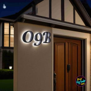 May include: Illuminated house number 09B in a modern font, mounted on a beige exterior wall. The numbers are dark grey with a bright white backlight, creating a striking contrast. The image is taken at night, with a wooden door visible.