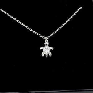 Puede incluir: Un collar de plata con un pequeño colgante de tortuga brillante. La tortuga está adornada con piedras de circonita cúbica transparentes.