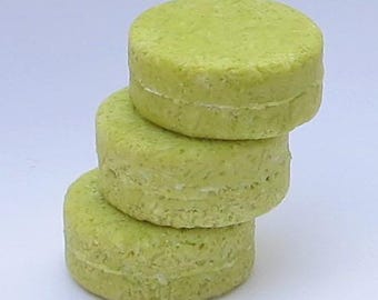May include: A stack of four round, green, solid shampoo bars. The bars are stacked on top of each other, with the top bar being the largest and the bottom bar being the smallest.