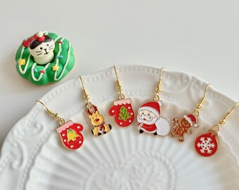 May include: A set of six gold Christmas-themed earrings with red, white, and green enamel. The earrings feature a reindeer, a mitten, a Christmas tree, Santa Claus, a gingerbread man, and a snowflake.