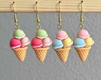 May include: Three pairs of gold ice cream cone earrings. Each earring features a cone with three scoops of ice cream in pink, green, and yellow or blue.