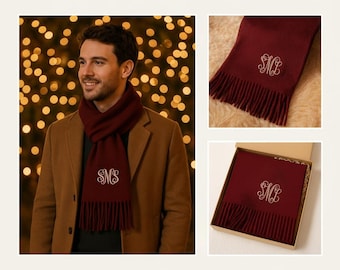 May include: A burgundy scarf with white embroidered initials and a fringed edge. The scarf is shown worn and boxed. The scarf is displayed on a person wearing a brown coat. The scarf is a winter accessory.