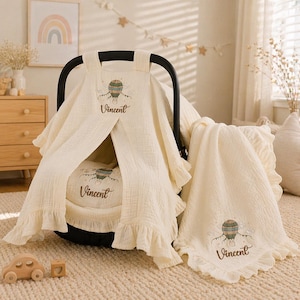 May include: Cream-coloured baby car seat cover and blanket set. The set features a hot air balloon design with the name "Vincent" embroidered on each piece. The cover has a ruffled edge.