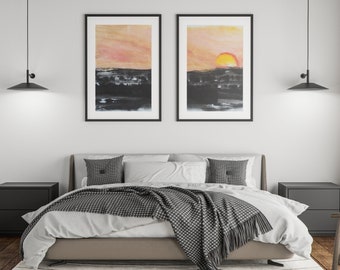Könnte beinhalten: Zwei gerahmte abstrakte Aquarellbilder eines Sonnenuntergangs über einer dunklen Landschaft. Das Bild rechts zeigt eine leuchtend orange Sonne. Die Bilder hängen an einer weißen Wand über einem Bett mit einer grau-weißen karierten Wolldecke.