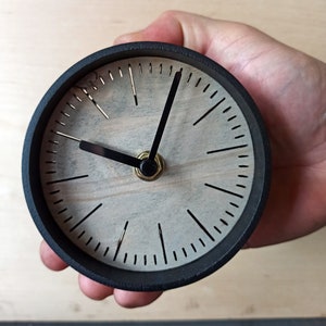 Könnte beinhalten: Eine schwarz-weiße Uhr mit schwarzen Zeigern. Das Zifferblatt der Uhr ist aus Holz und hat ein schlichtes Design.