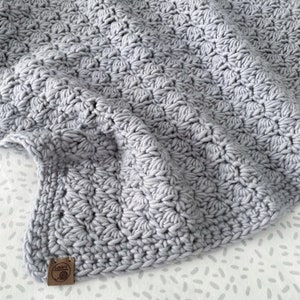 May include: A soft, gray crocheted baby blanket with a small brown tag that says "Loopy Threads".