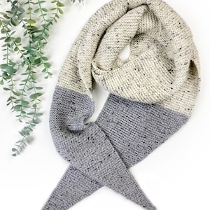 May include: A knitted scarf with a two-tone color scheme. The scarf is mostly white with black flecks, and the bottom half is a solid gray.