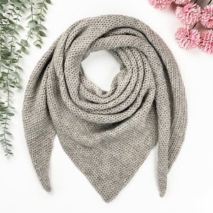 May include: A gray knitted triangular scarf with a textured pattern. The scarf is folded in half and laid flat on a white background.
