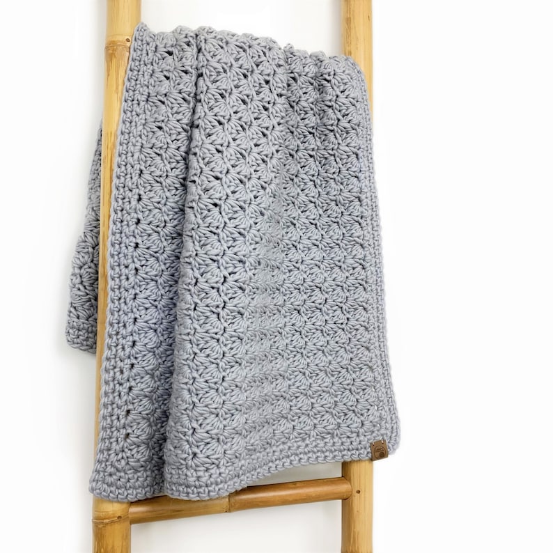 May include: A gray crocheted baby blanket hanging on a wooden ladder. The blanket has a delicate, lacy pattern.