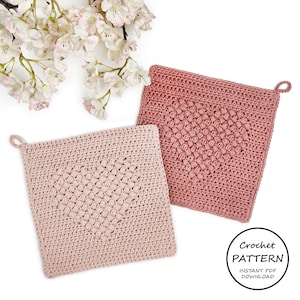 Può includere: Due presine da forno rosa all'uncinetto con un design a forma di cuore. Le presine sono su uno sfondo bianco con fiori di ciliegio rosa.