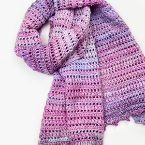 May include: A hand-crocheted scarf featuring a variegated yarn pattern in shades of magenta, lavender, and soft purple. The accessory displays a textured stitch design with alternating rows of openwork and dense clusters, finished with a scalloped edge.