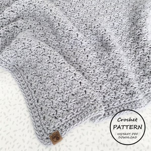 May include: A gray crochet blanket with a textured stitch pattern. The blanket is folded and has a brown leather tag with the word "Loops" on it. The text "Crochet Pattern Instant PDF Download" is also visible in the image.